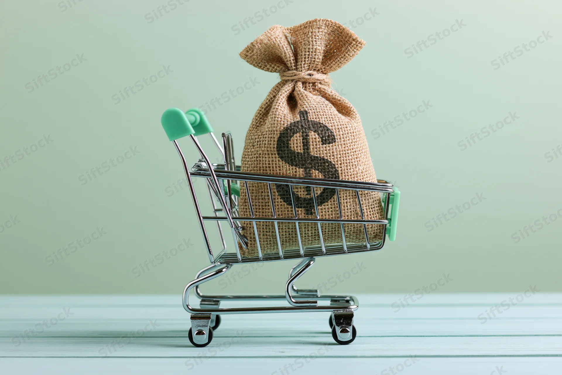 Burlap money bag with dollar sign in miniature shopping cart on wooden surface