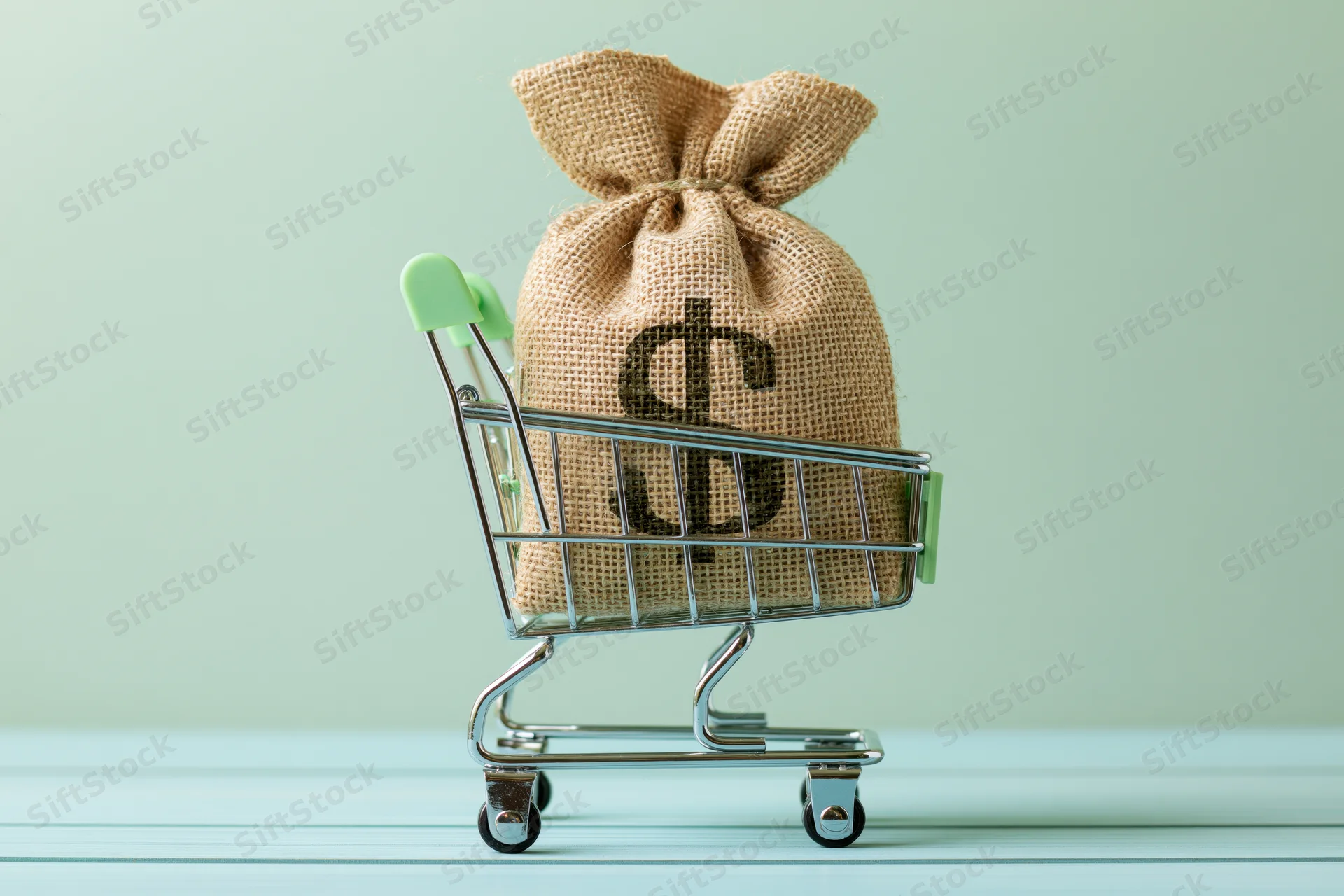 Burlap money bag with dollar sign in miniature shopping cart on light surface
