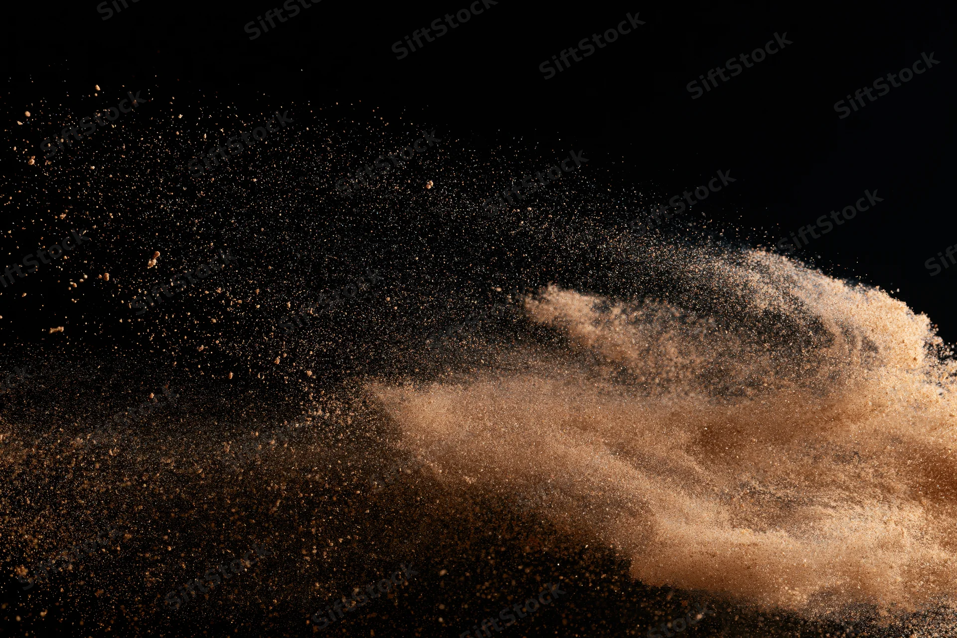 Fine desert sand bursting mid-air in dynamic explosion against black background