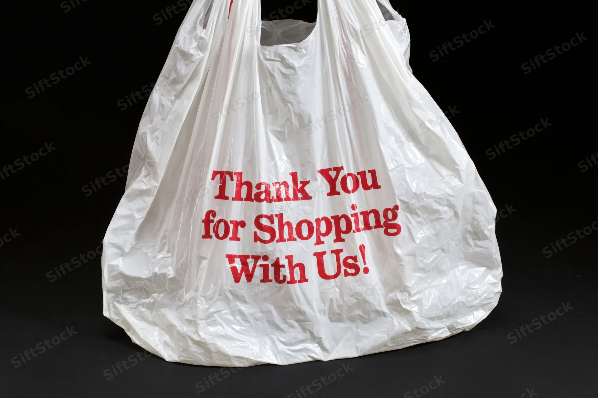 Crinkled white plastic shopping bag with red text thank you for shopping with us on black background