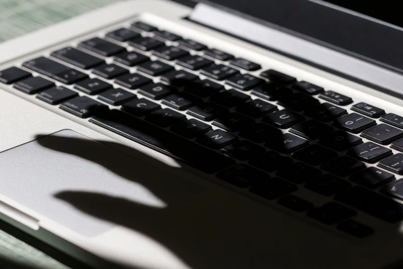 Shadow of a hand cast across a laptop keyboard on a desk