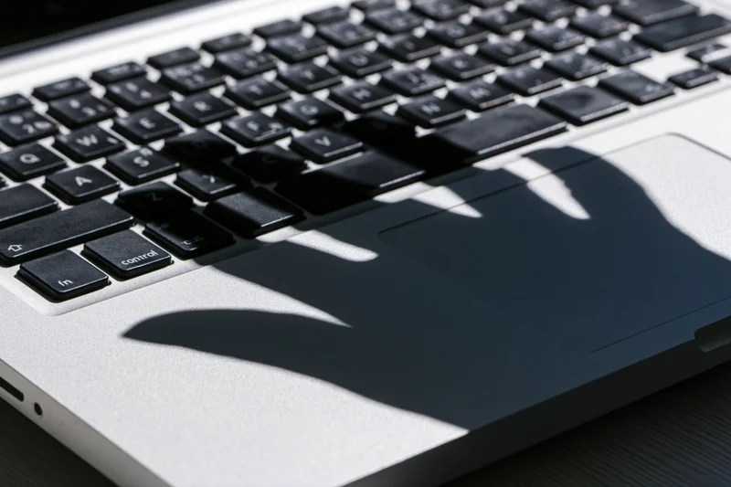 Shadow of a hand cast across a laptop keyboard in bright sunlight