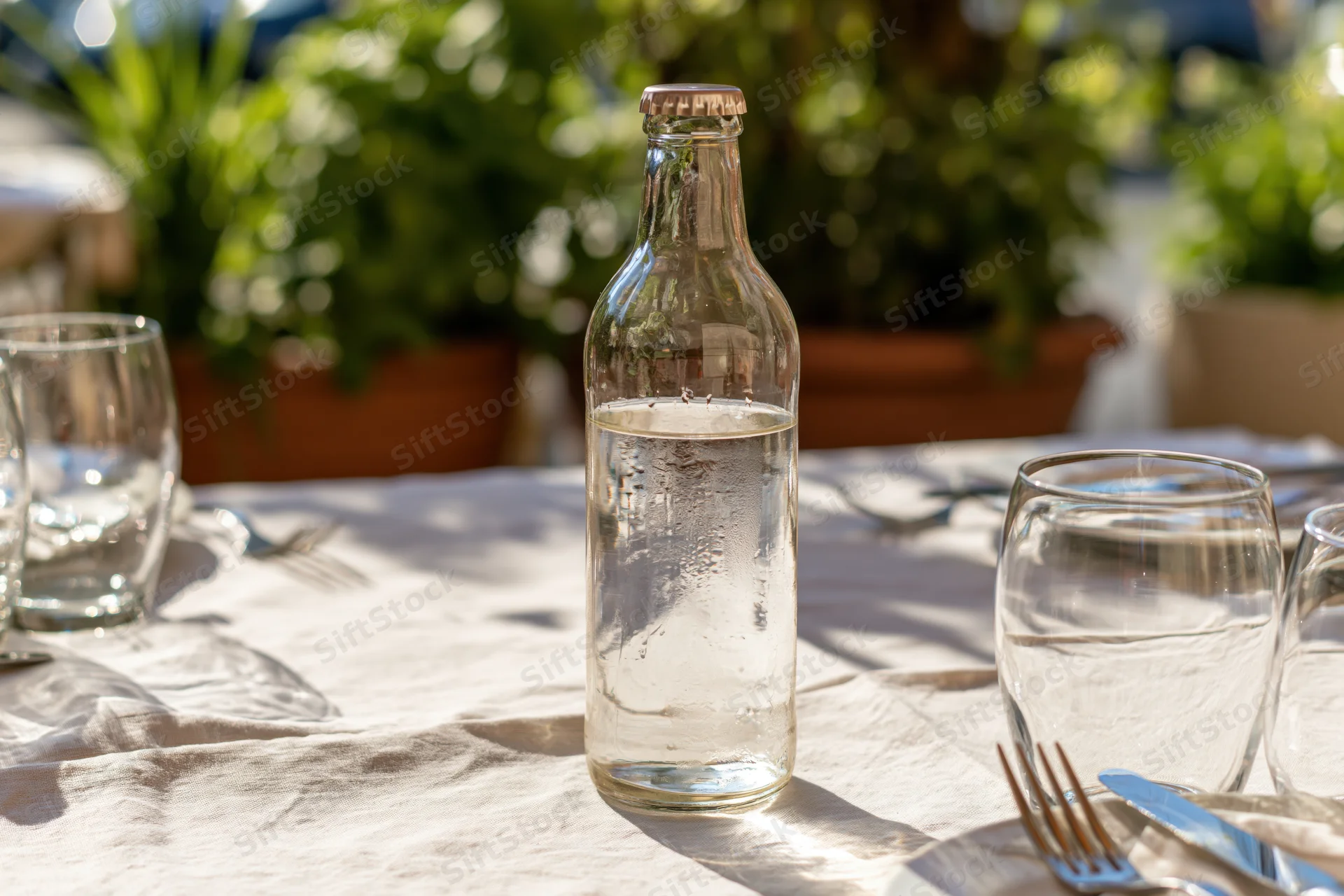 Glass water bottle with condensation on a set outdoor restaurant table with cutlery and glassware