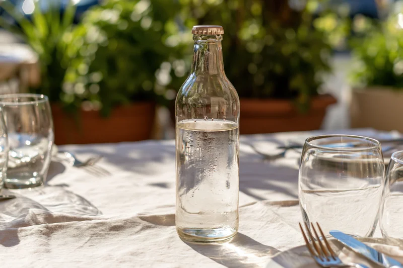 Glass water bottle with condensation on a set outdoor restaurant table with cutlery and glassware