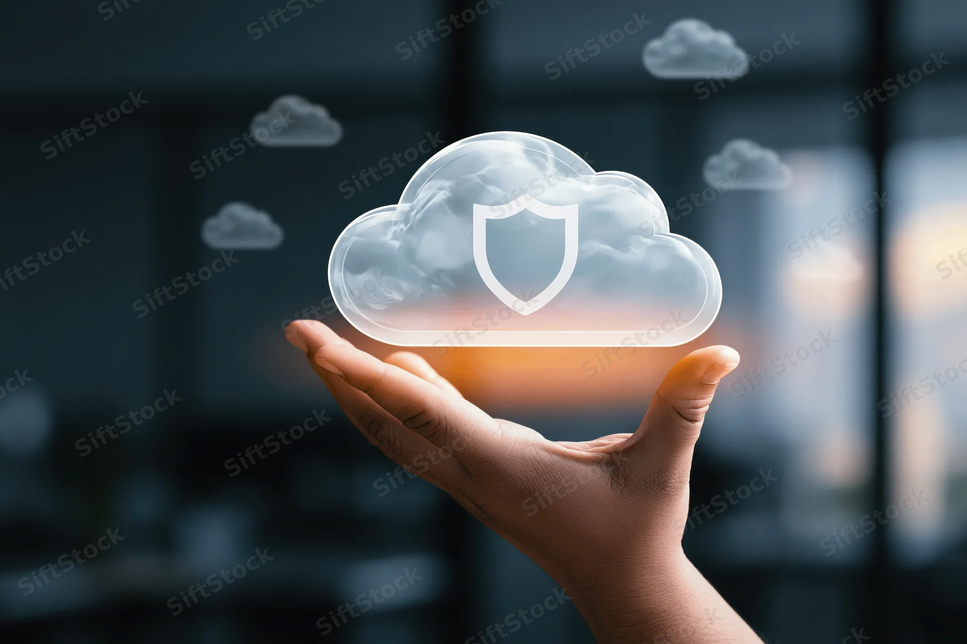 Hand holding a glowing translucent cloud with a shield symbol over a blurred office background