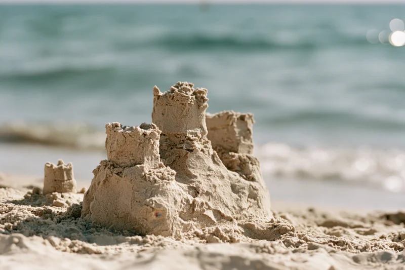 Handmade sandcastle with three uneven towers on a sandy beach near the ocean