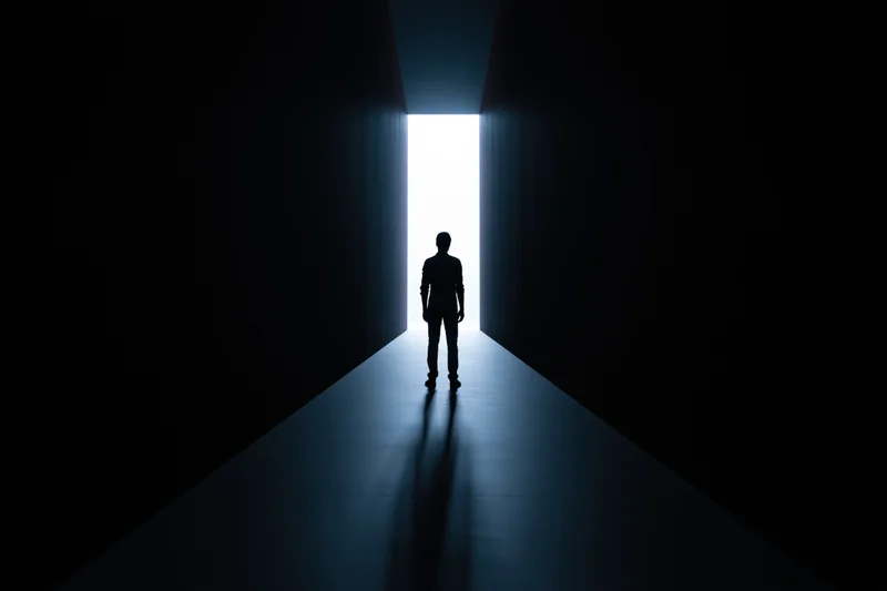 Silhouette of a man standing still at the end of a dark hallway facing bright light