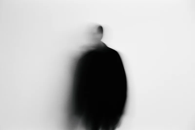 Blurred silhouette of a person standing against a plain light background