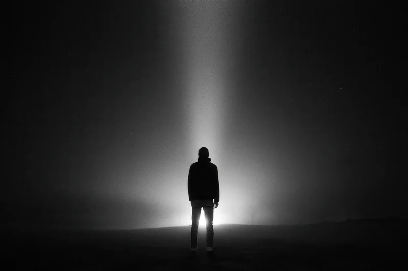 Silhouette of a person standing alone in a dark landscape illuminated by a vertical beam of light from above