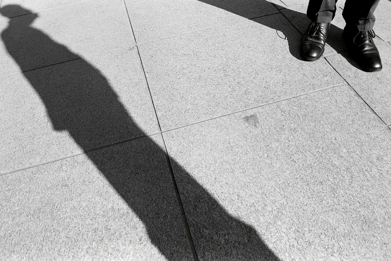 Long shadow of a standing man cast across grey pavement in urban setting