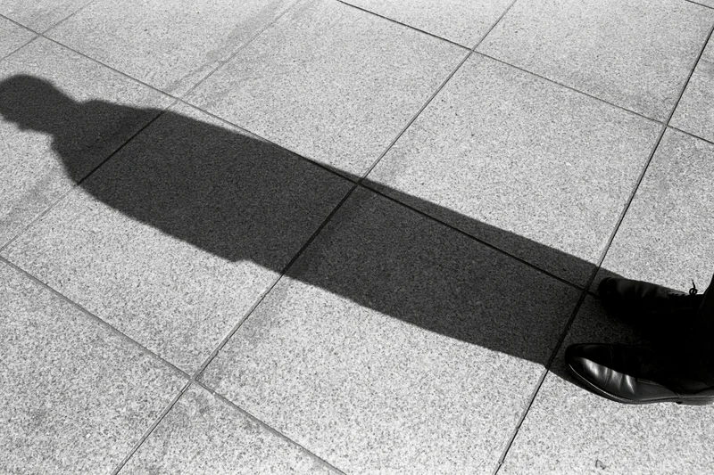 Long shadow of a standing person cast across tiled pavement in black and white