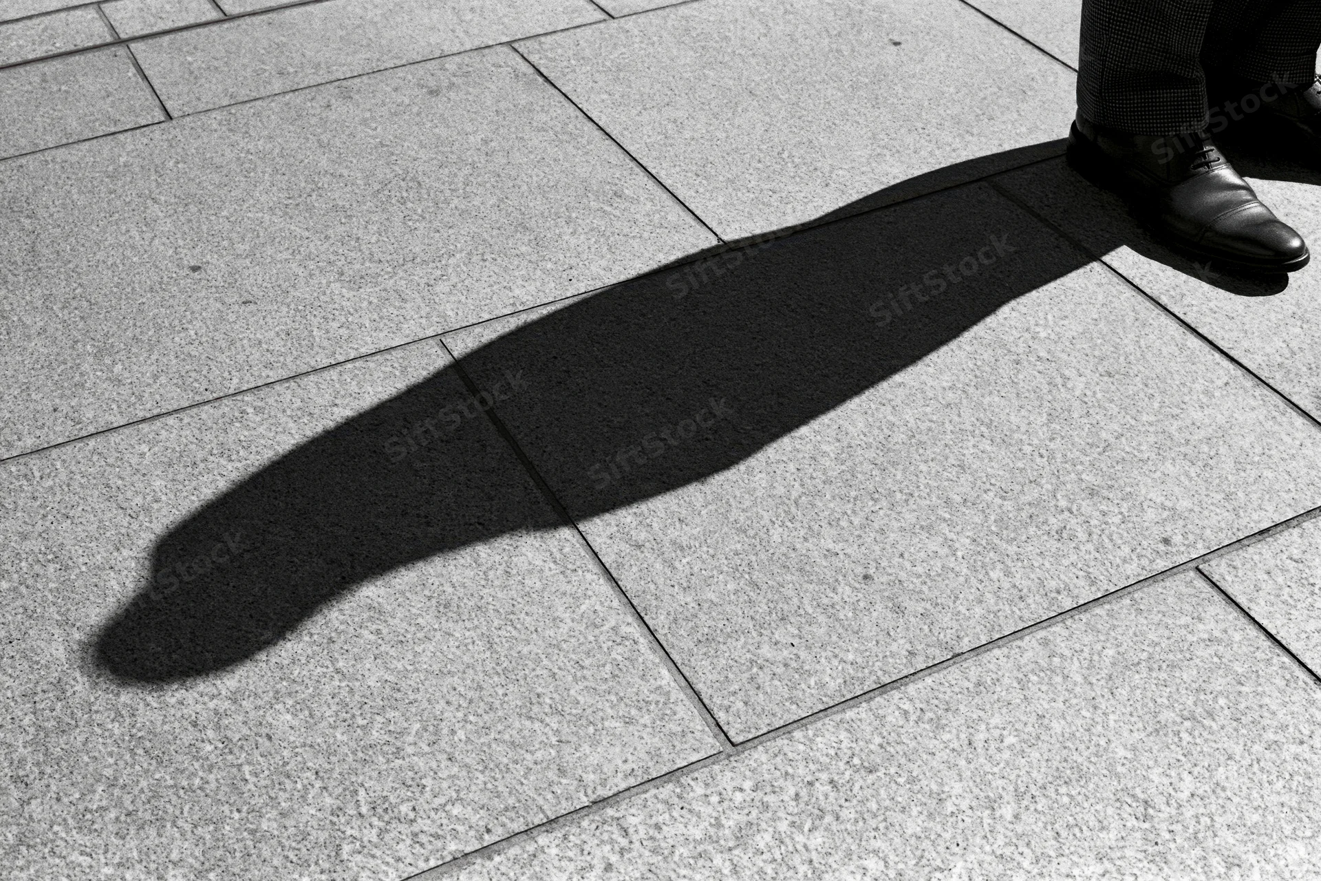 Long shadow of a standing person cast across grey pavement in urban setting
