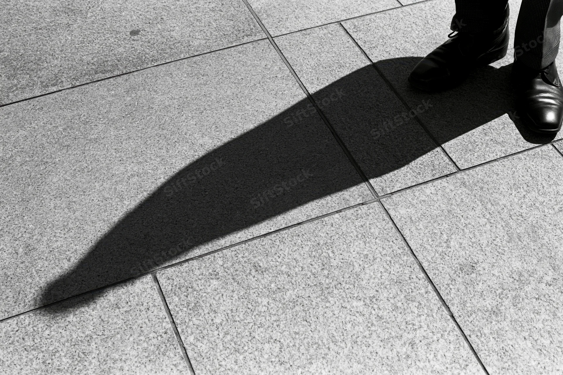 Long shadow of a standing person cast across grey pavement in urban setting