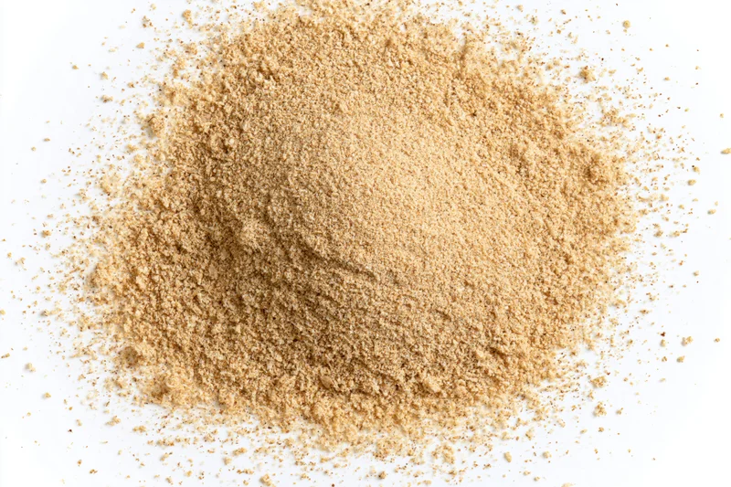 A mound of fine beige spice powder scattered on a white surface
