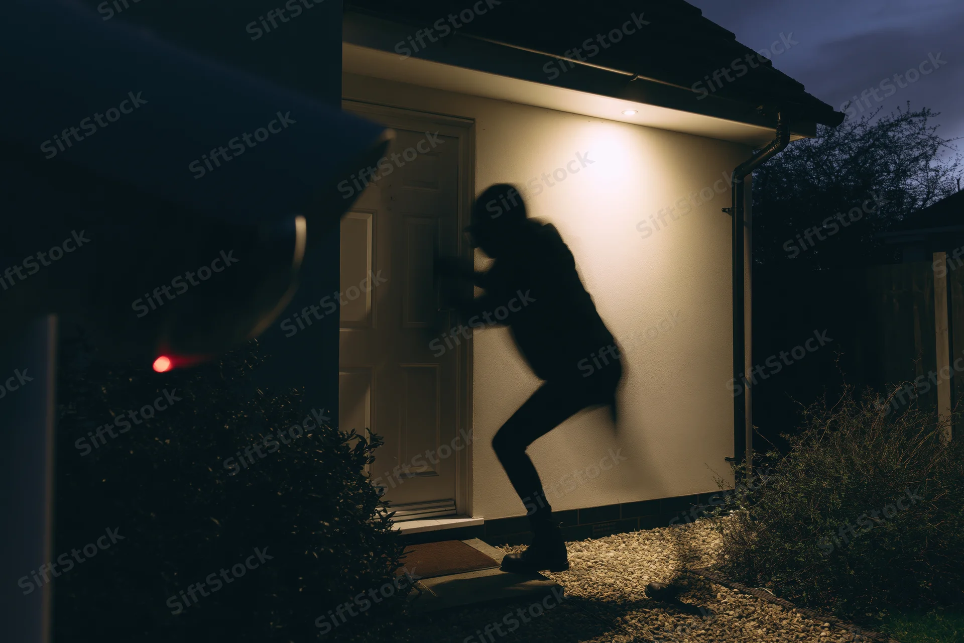 Silhouette of intruder breaking into house door at night under porch light