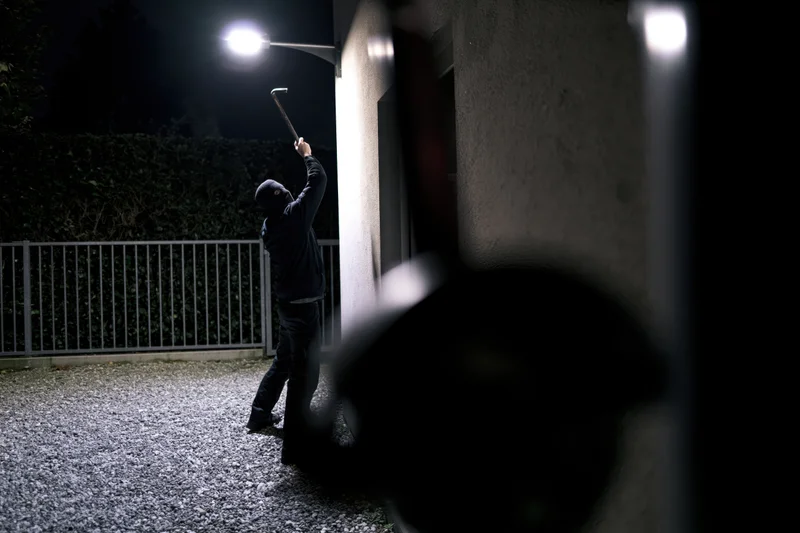 Masked burglar raising crowbar at house entrance at night