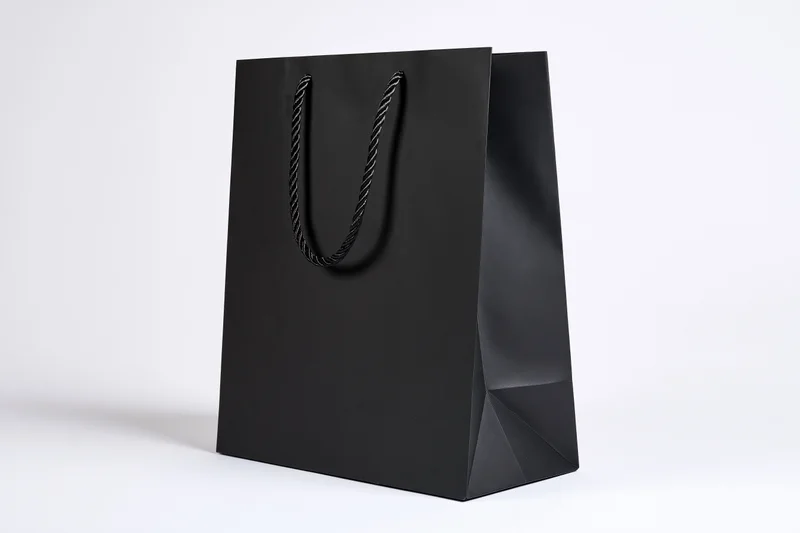 Matte black paper shopping bag with twisted rope handles on white background