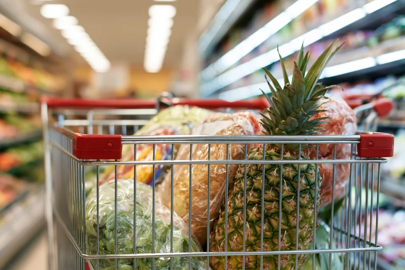 Metal shopping cart filled with groceries in supermarket aisle