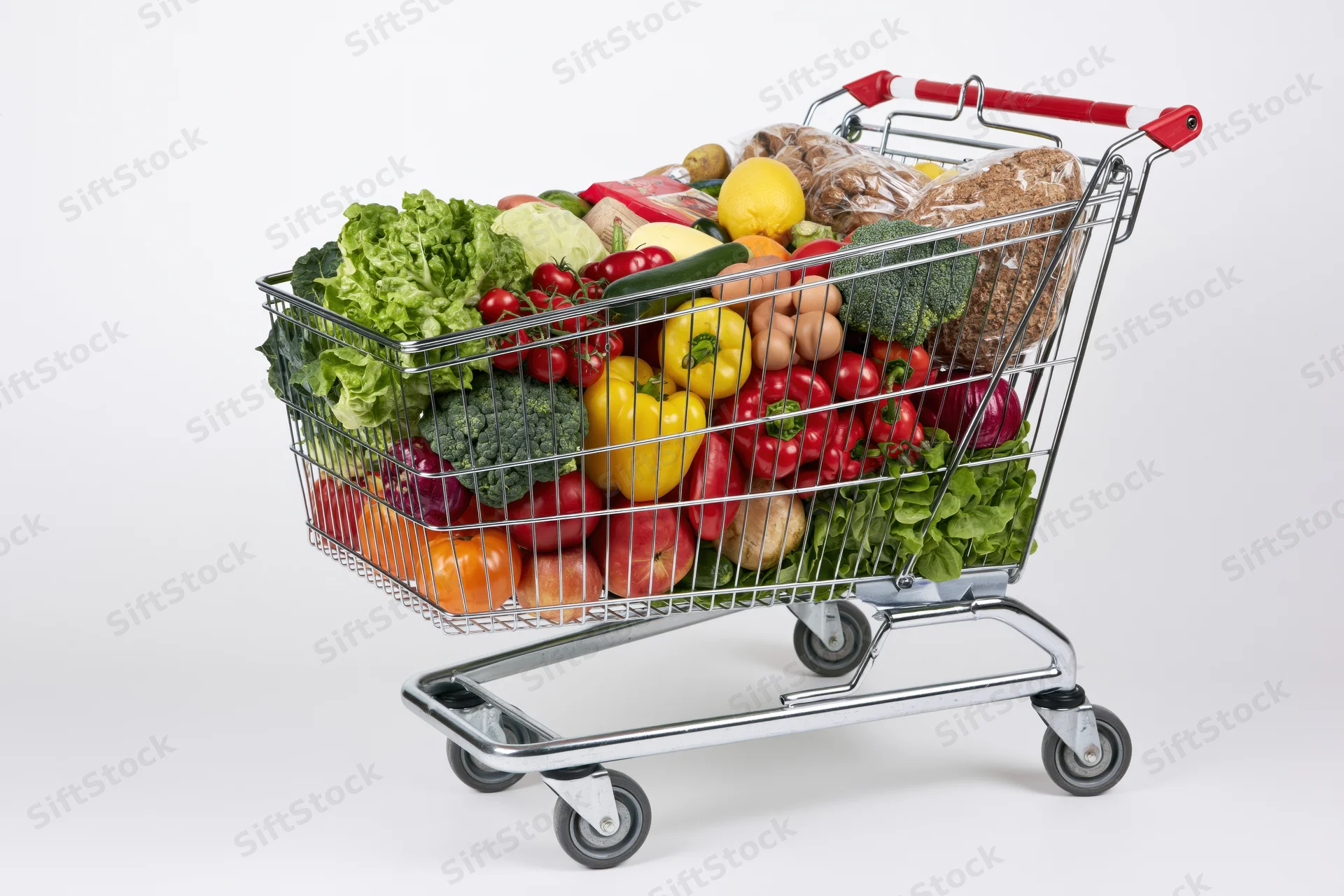 Metal shopping cart filled with fresh vegetables and fruits on white background