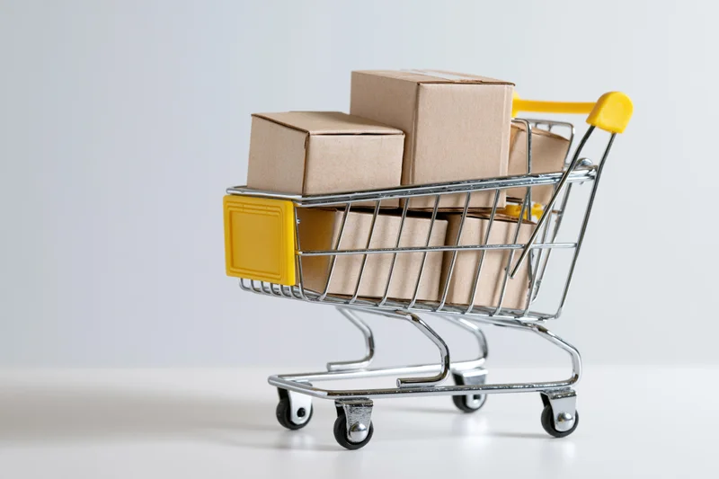 Miniature metal shopping cart filled with cardboard boxes on white surface