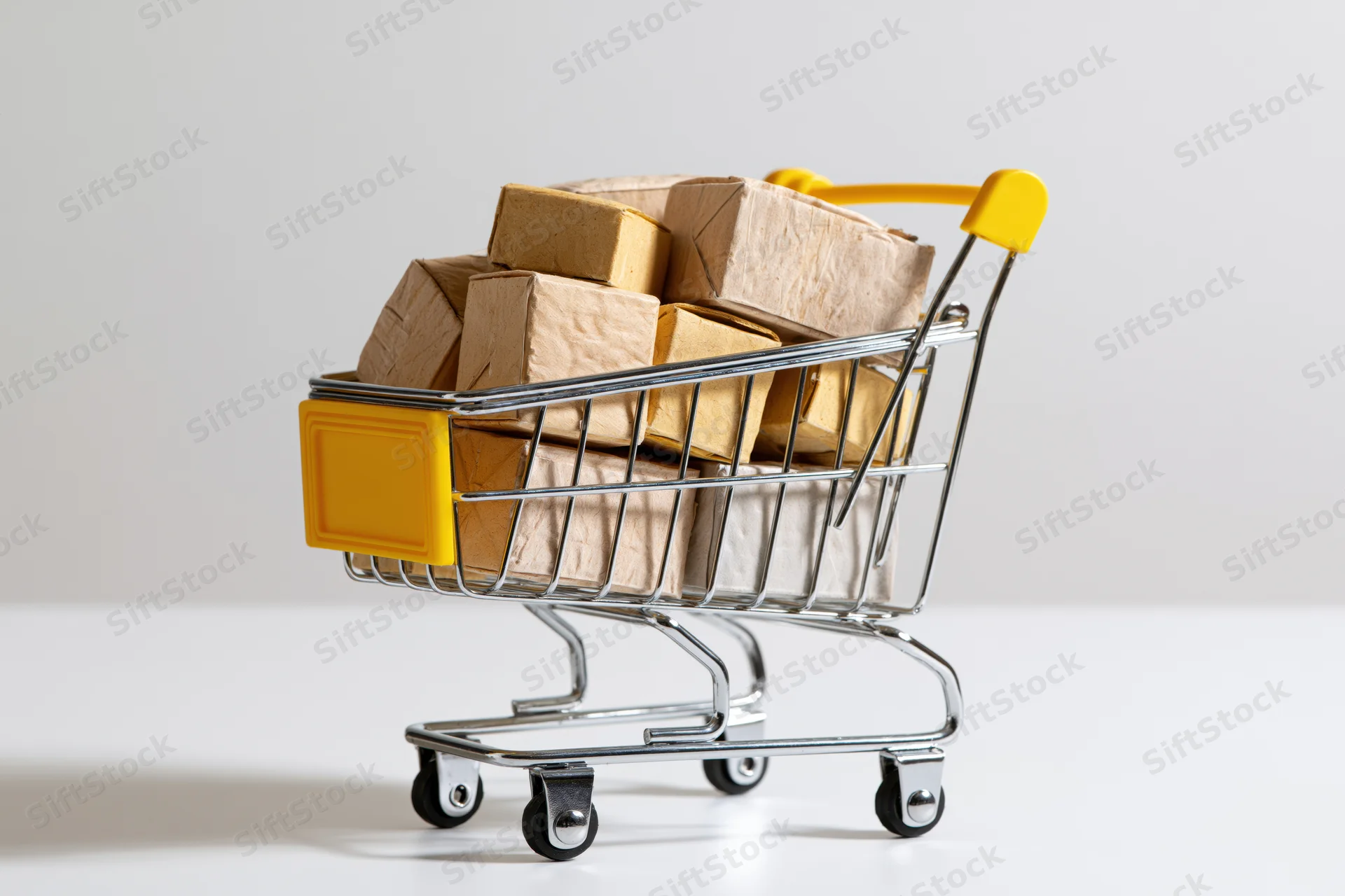 Miniature metal shopping cart filled with cardboard boxes on white surface