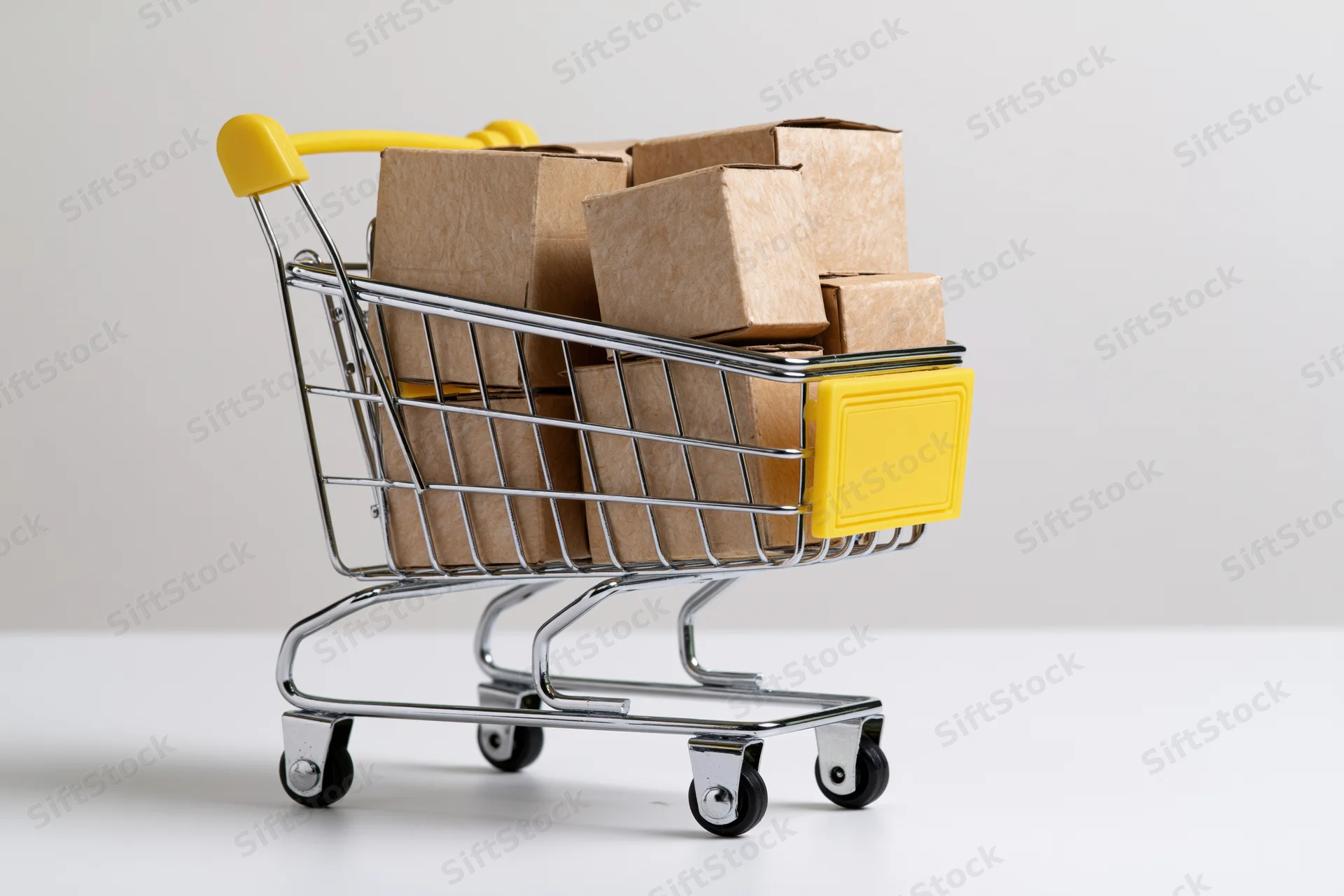Miniature shopping cart filled with cardboard boxes on white surface