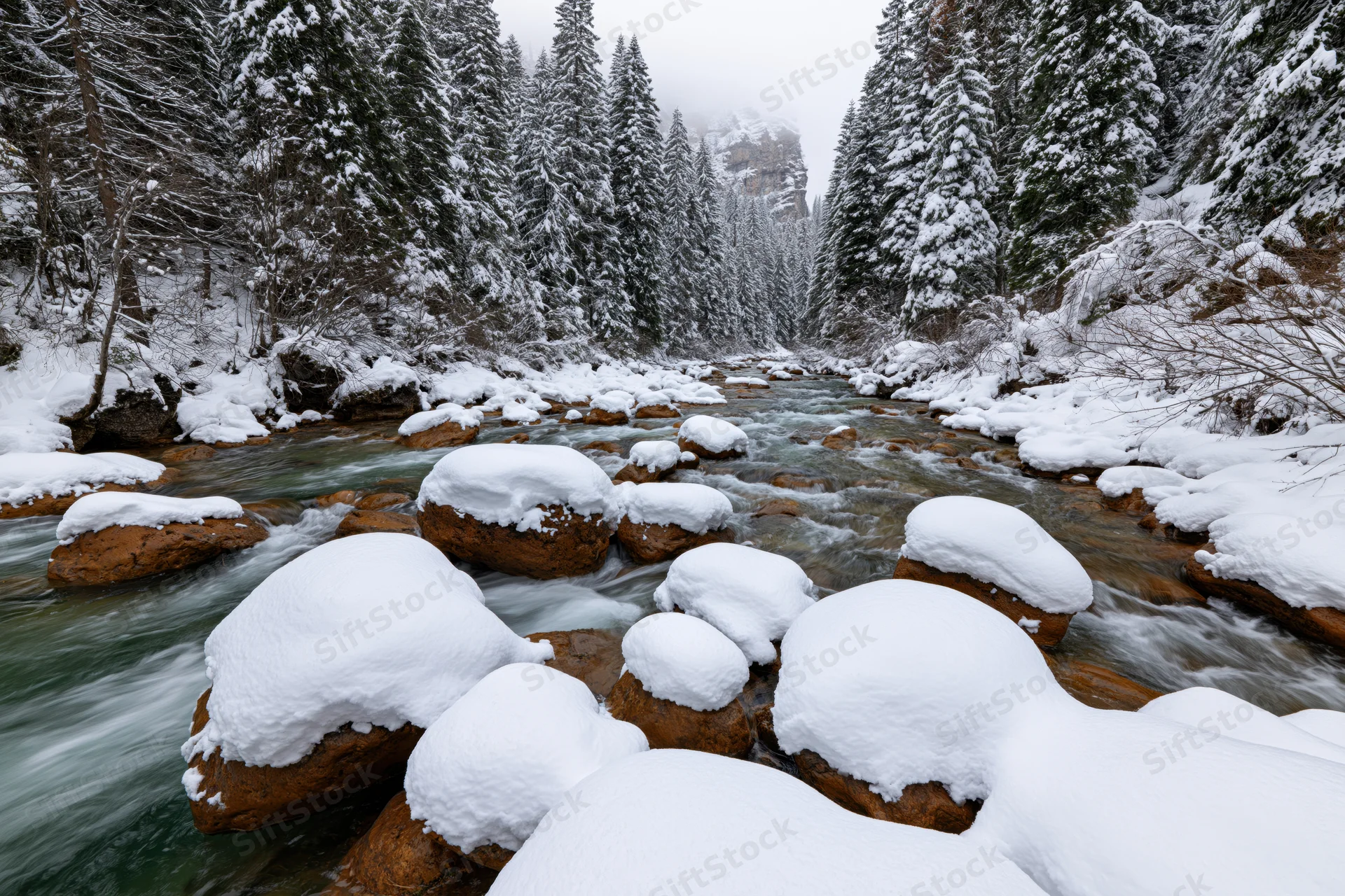 Snow-covered river flowing over amber rocks in a pine forest valley