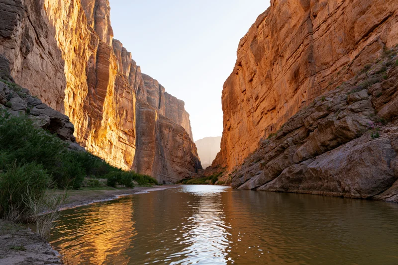 River flowing through narrow desert canyon with towering sandstone cliffs at sunrise