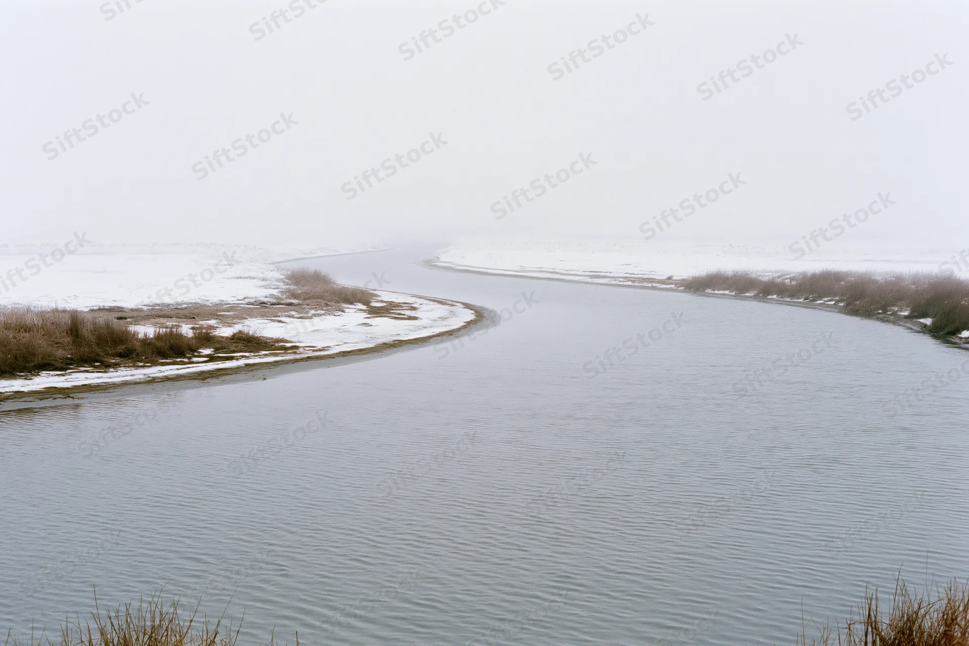 Winding river flowing through snow-covered landscape under overcast sky