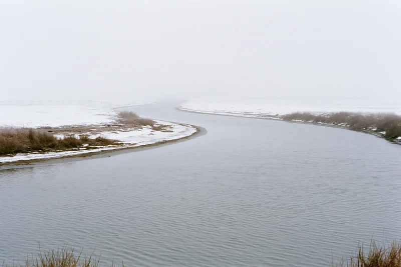 Winding river flowing through snow-covered landscape under overcast sky