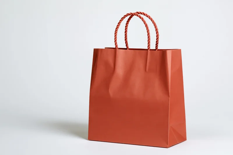 Red-orange kraft paper shopping bag with twisted rope handles on white background