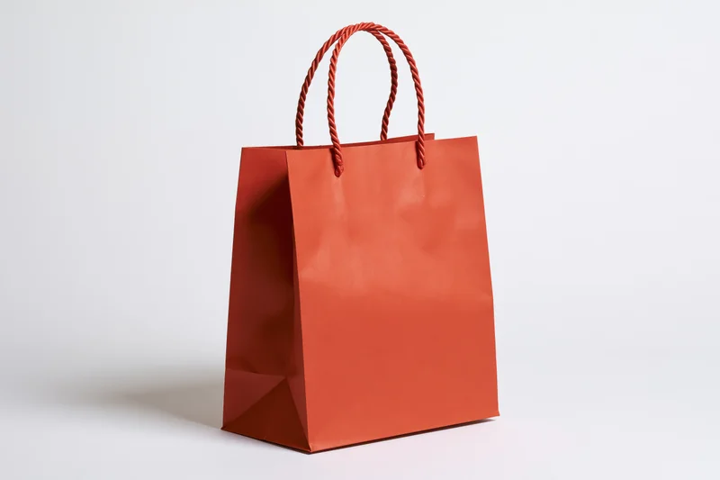 Red-orange kraft paper shopping bag with twisted rope handles on white background