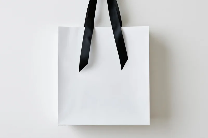 White paper shopping bag with black ribbon handles against plain background