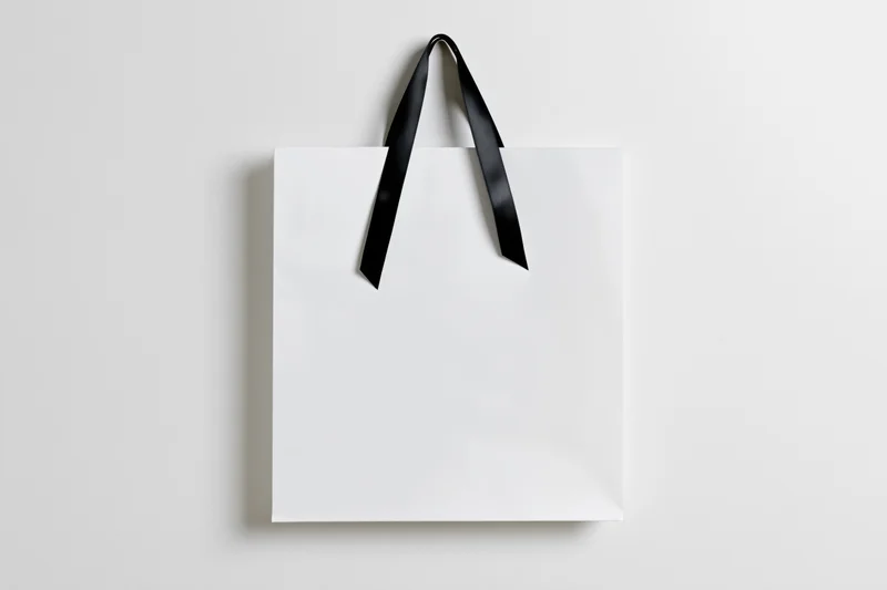 White paper shopping bag with black ribbon handles on plain background