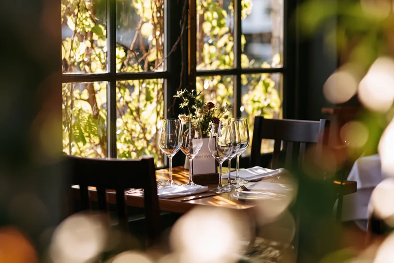 Reserved restaurant table set with wine glasses and flowers by a sunlit window