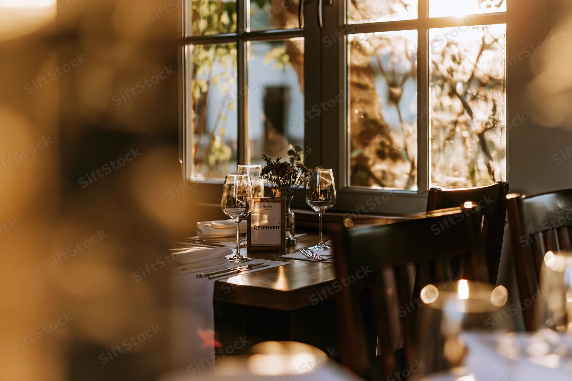 Reserved restaurant table set with wine glasses and candlelit ambiance by a window
