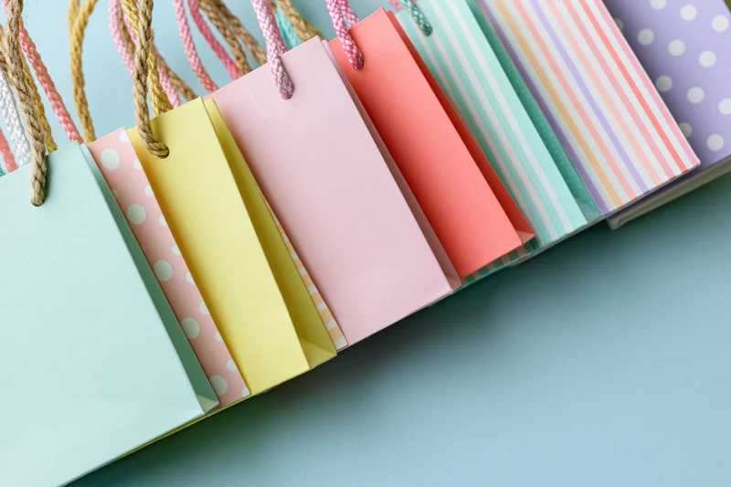 Row of small colorful paper shopping bags with rope handles on blue surface
