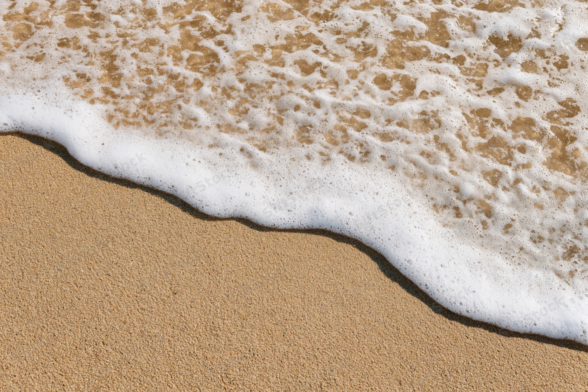 Shallow ocean wave washing over wet beach sand with white seafoam