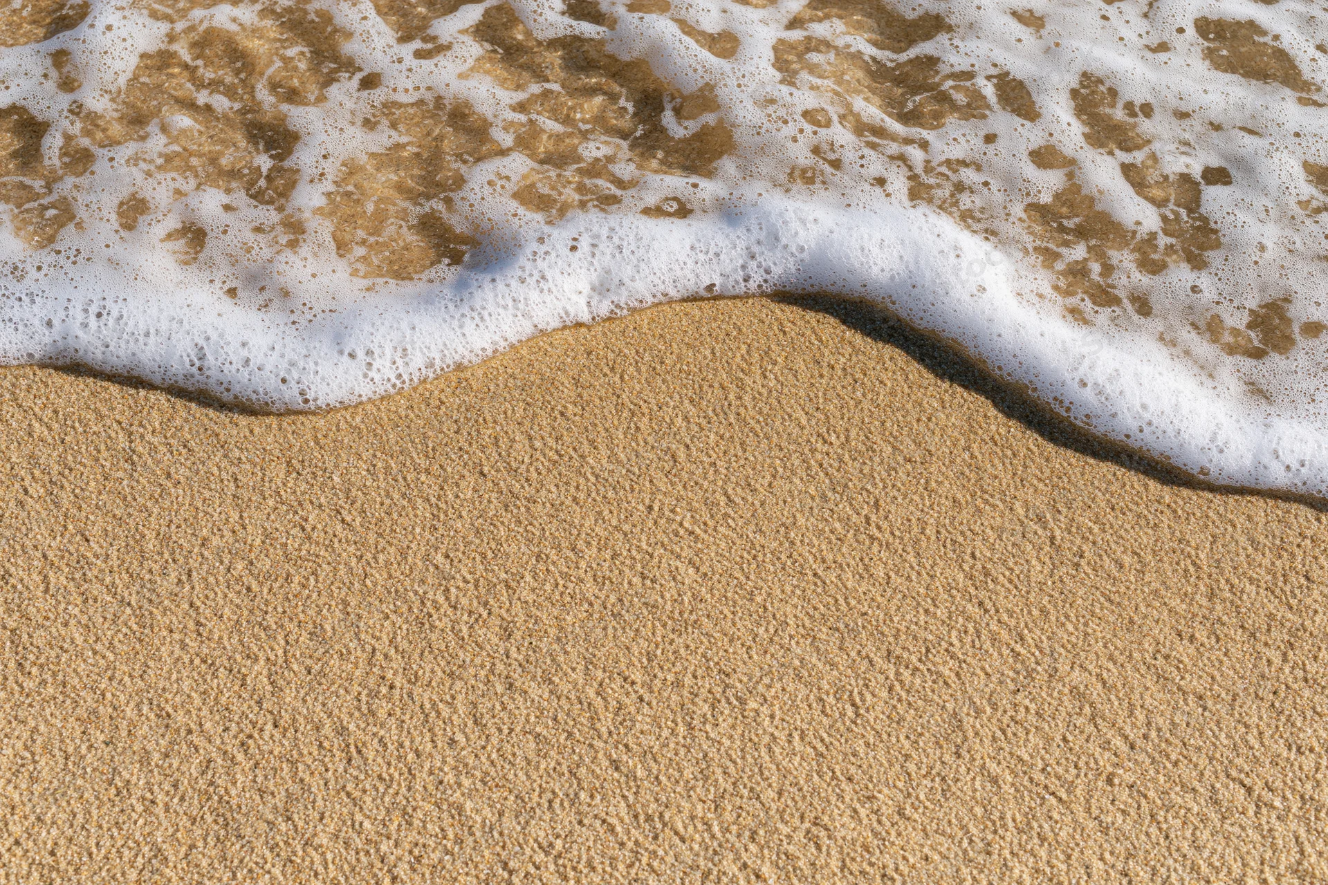 Shallow ocean wave washing over wet beach sand with white seafoam