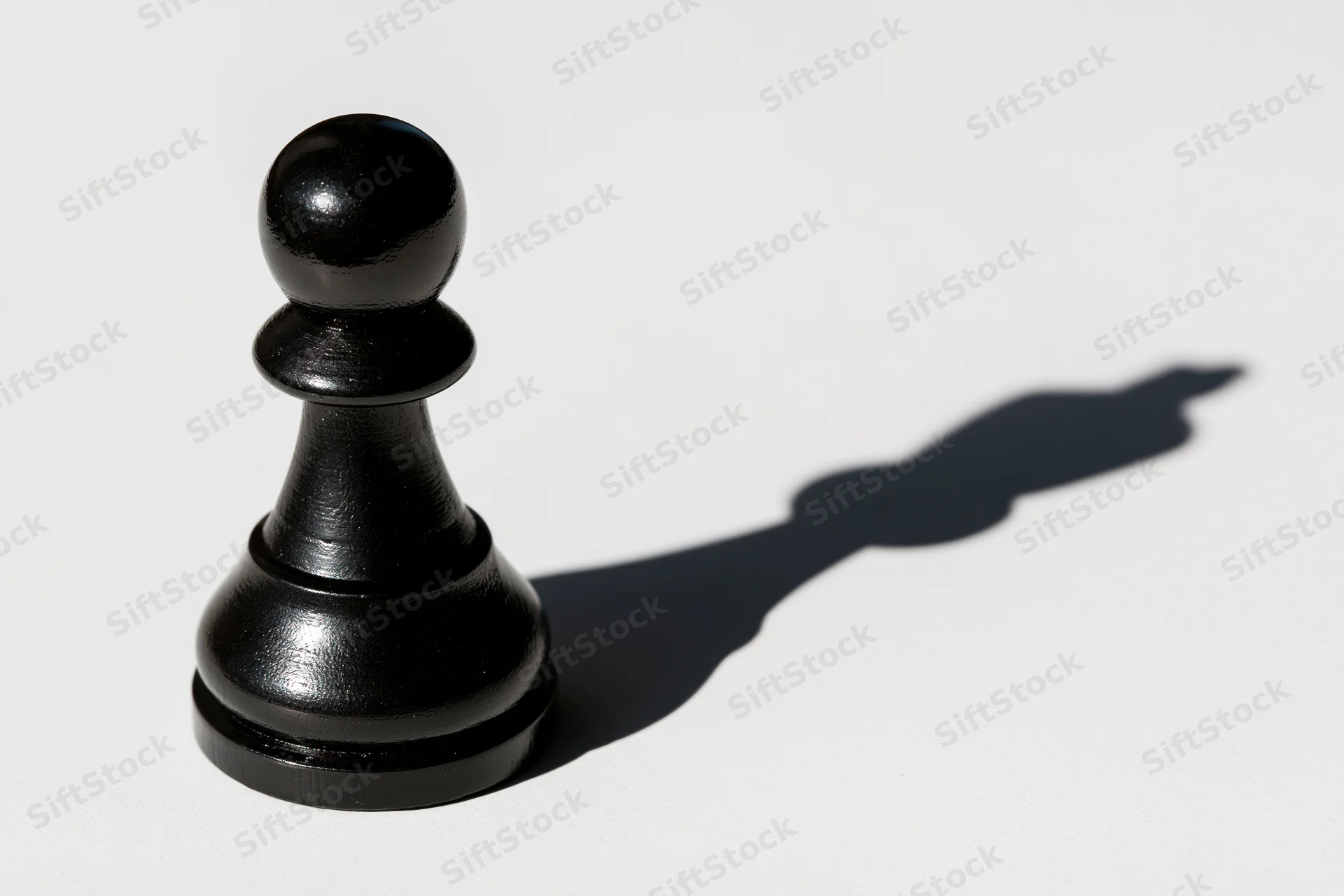 Black chess pawn standing upright on white surface casting a long shadow