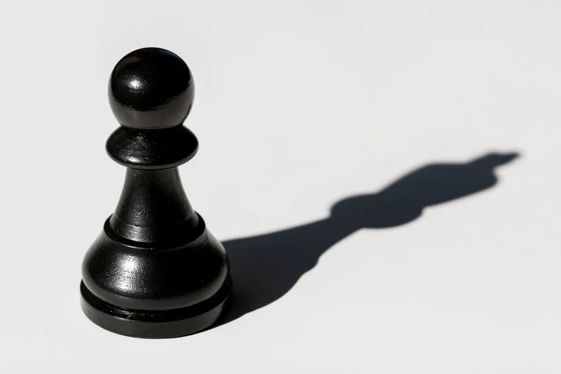Black chess pawn standing upright on white surface casting a long shadow