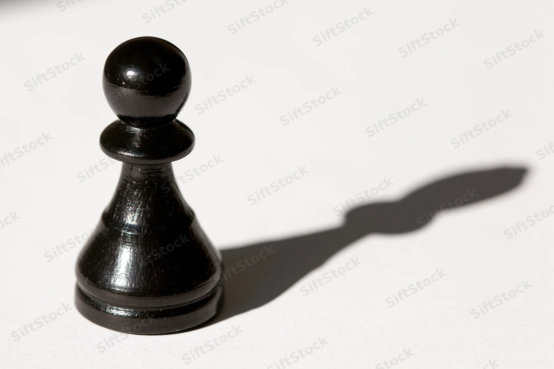 Black chess pawn standing upright on white surface casting a shadow