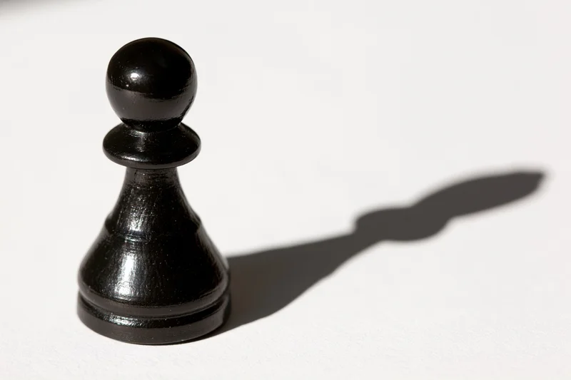 Black chess pawn standing upright on white surface casting a shadow