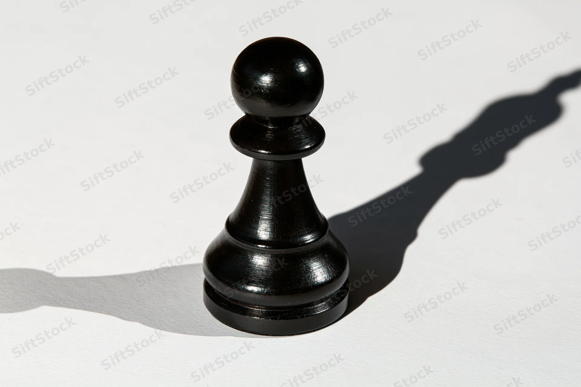 Black chess pawn standing upright on white surface casting a shadow