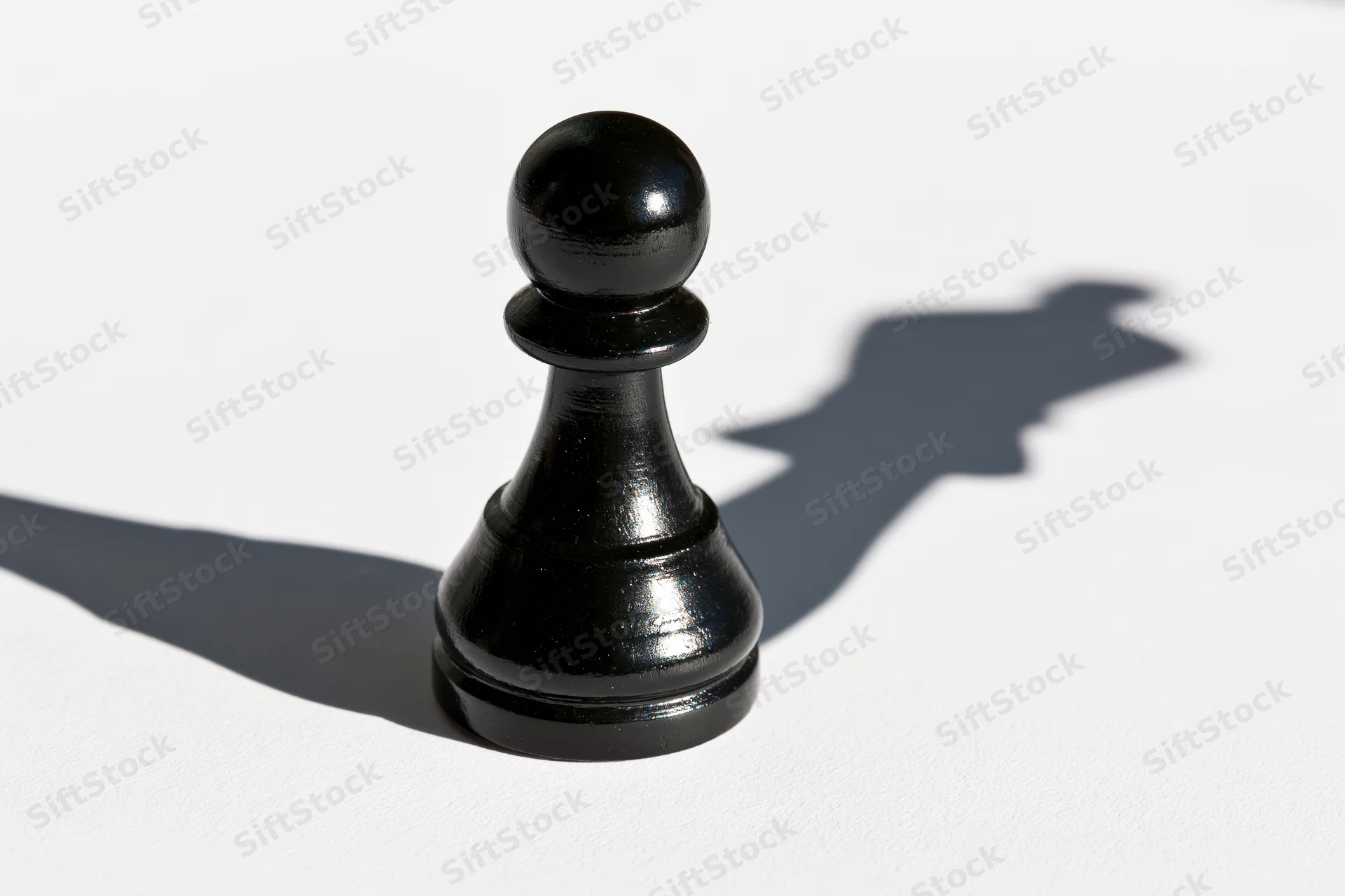 Black chess pawn standing upright on white surface casting a shadow