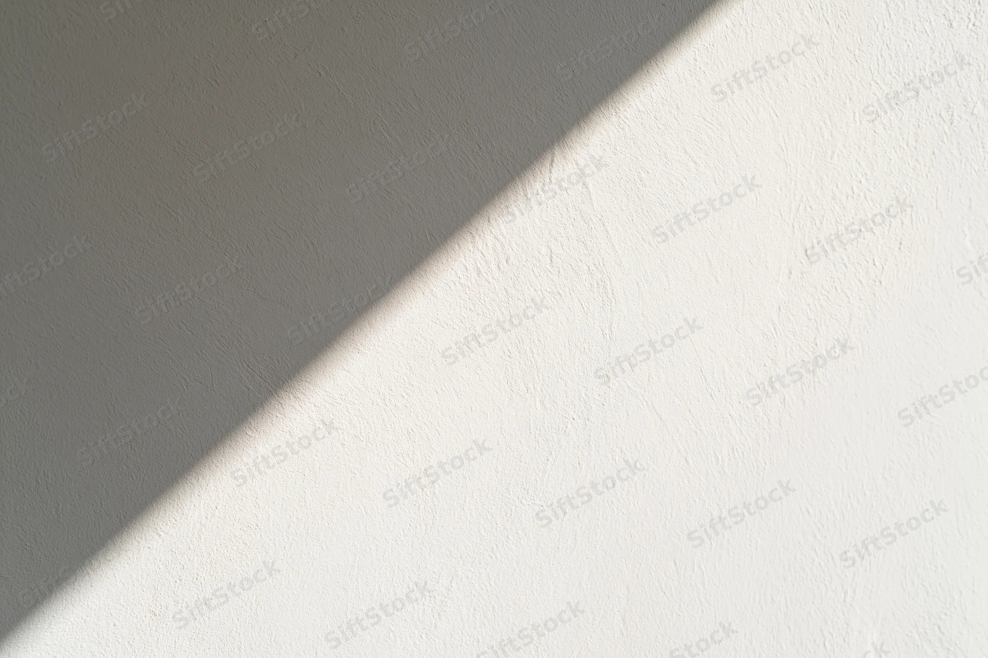 Diagonal band of sunlight across a white textured wall in an interior space