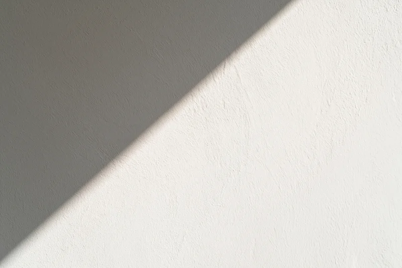 Diagonal band of sunlight across a white textured wall in an interior space