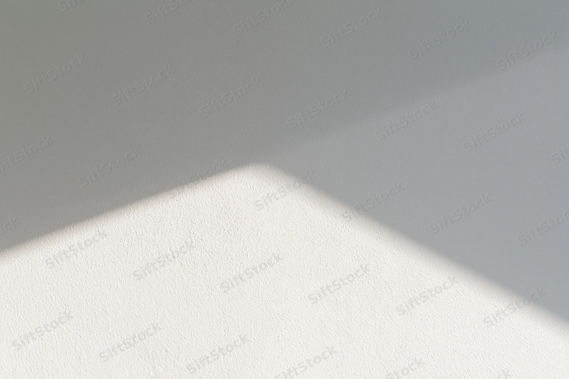 Diagonal band of sunlight across a white textured wall in an empty interior space