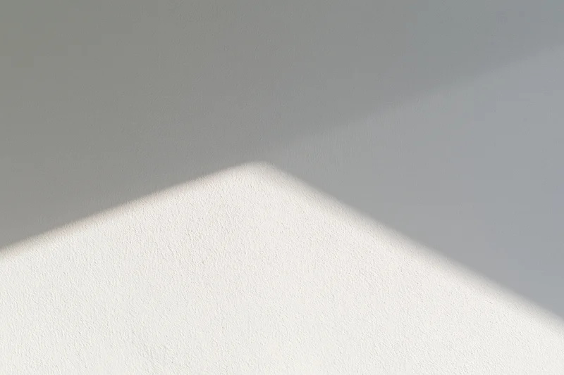 Diagonal band of sunlight across a white textured wall in an empty interior space