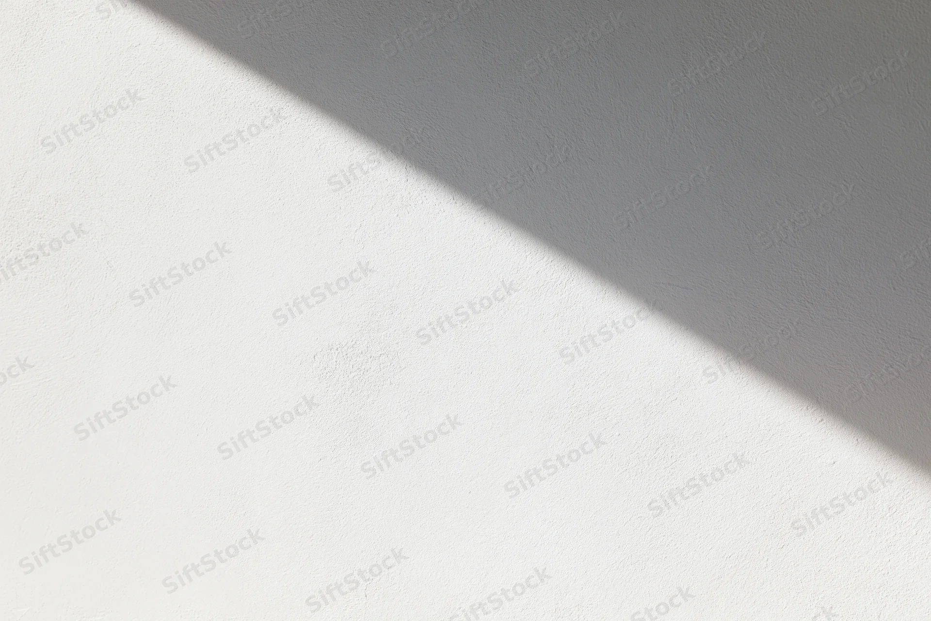 Diagonal sunlight casting shadow across white textured wall interior